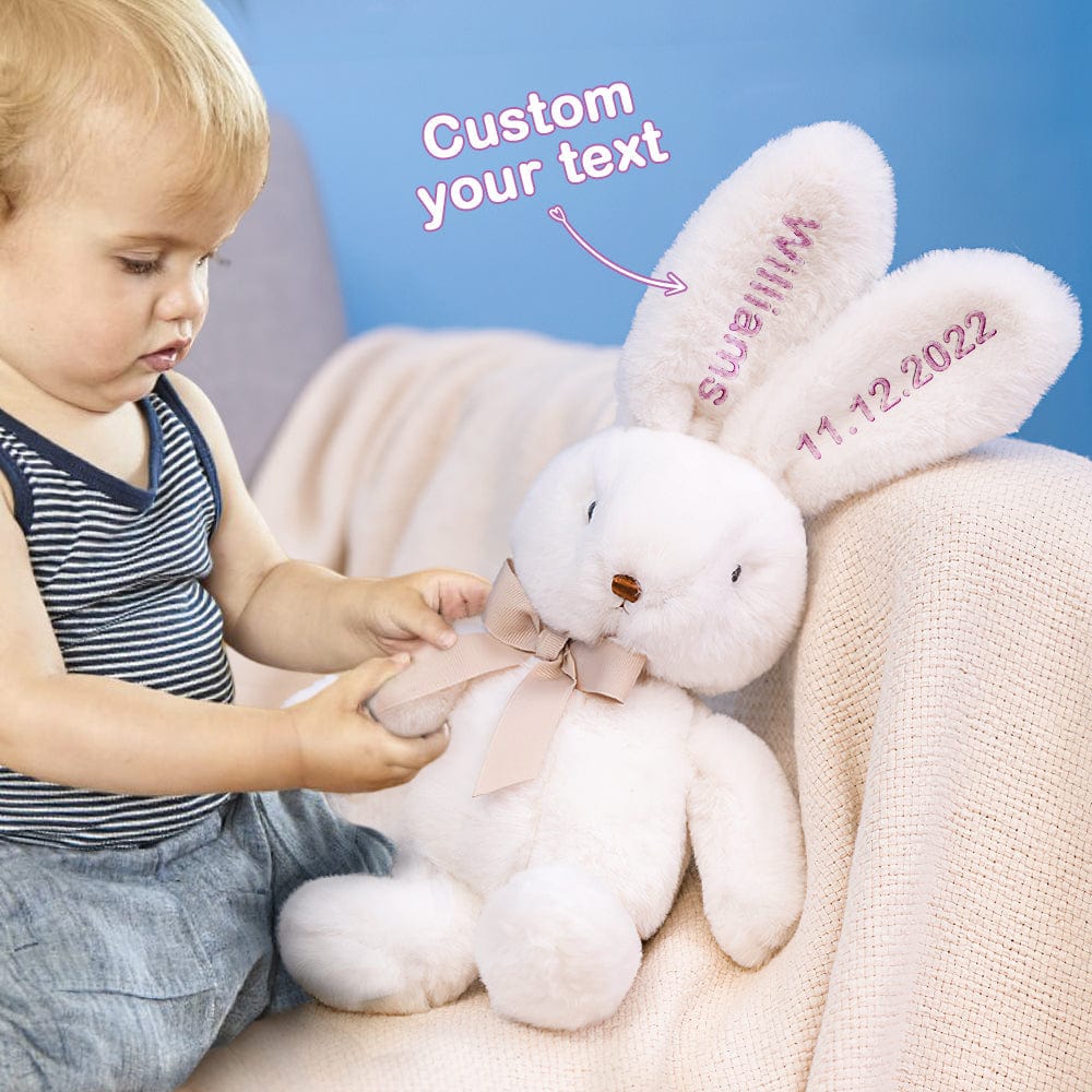 Toddler playing with a bunny’s bow – A child interacting with a white bunny that has pink embroidery and a matching bow.