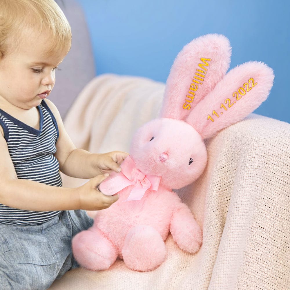 Toddler engaging with a plush bunny – A child playing with the bow of a pink bunny that has yellow embroidery.