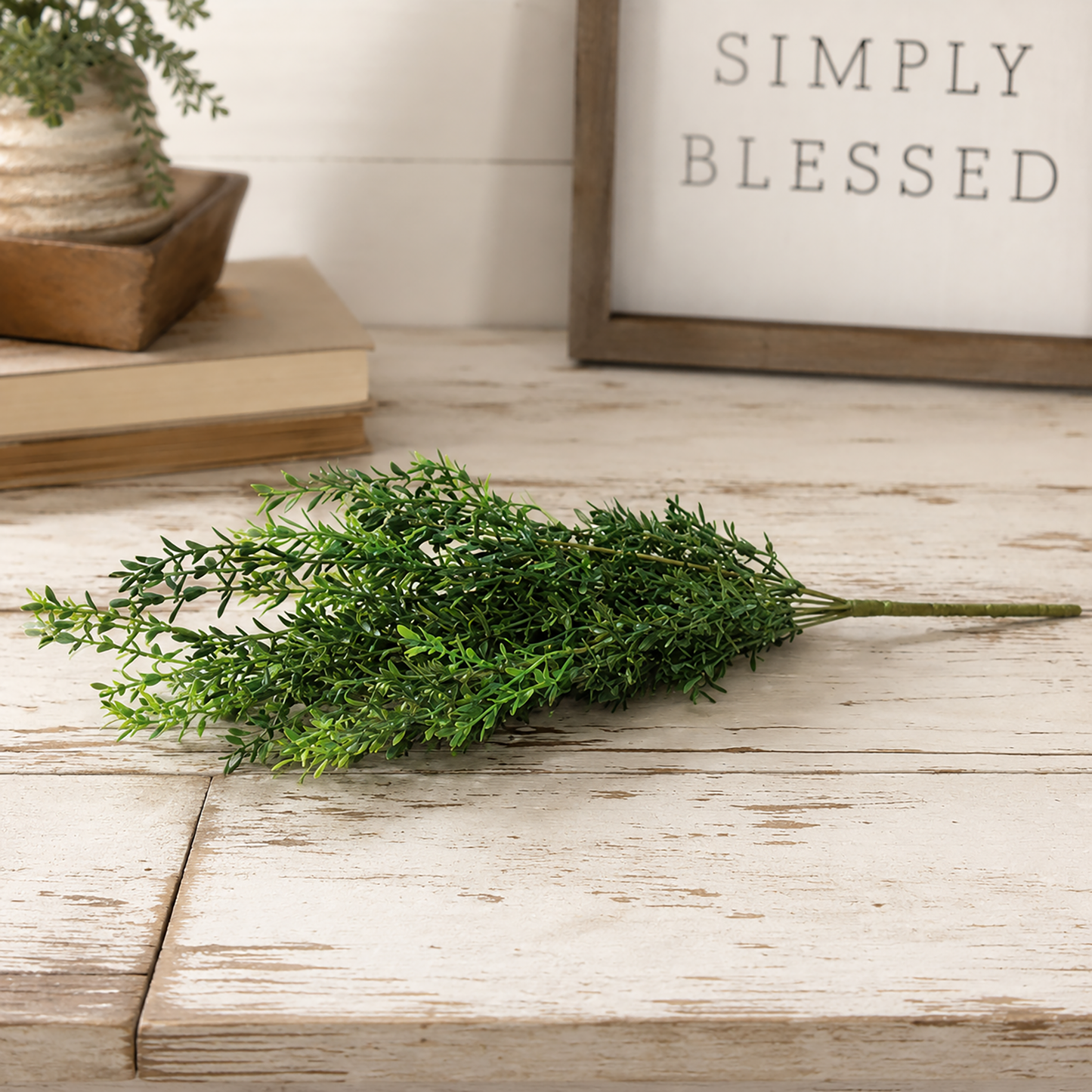 New England boxwood bush laid across a rustic farmhouse table with books, greenery, and a framed wall sign in a bright neutral setting.