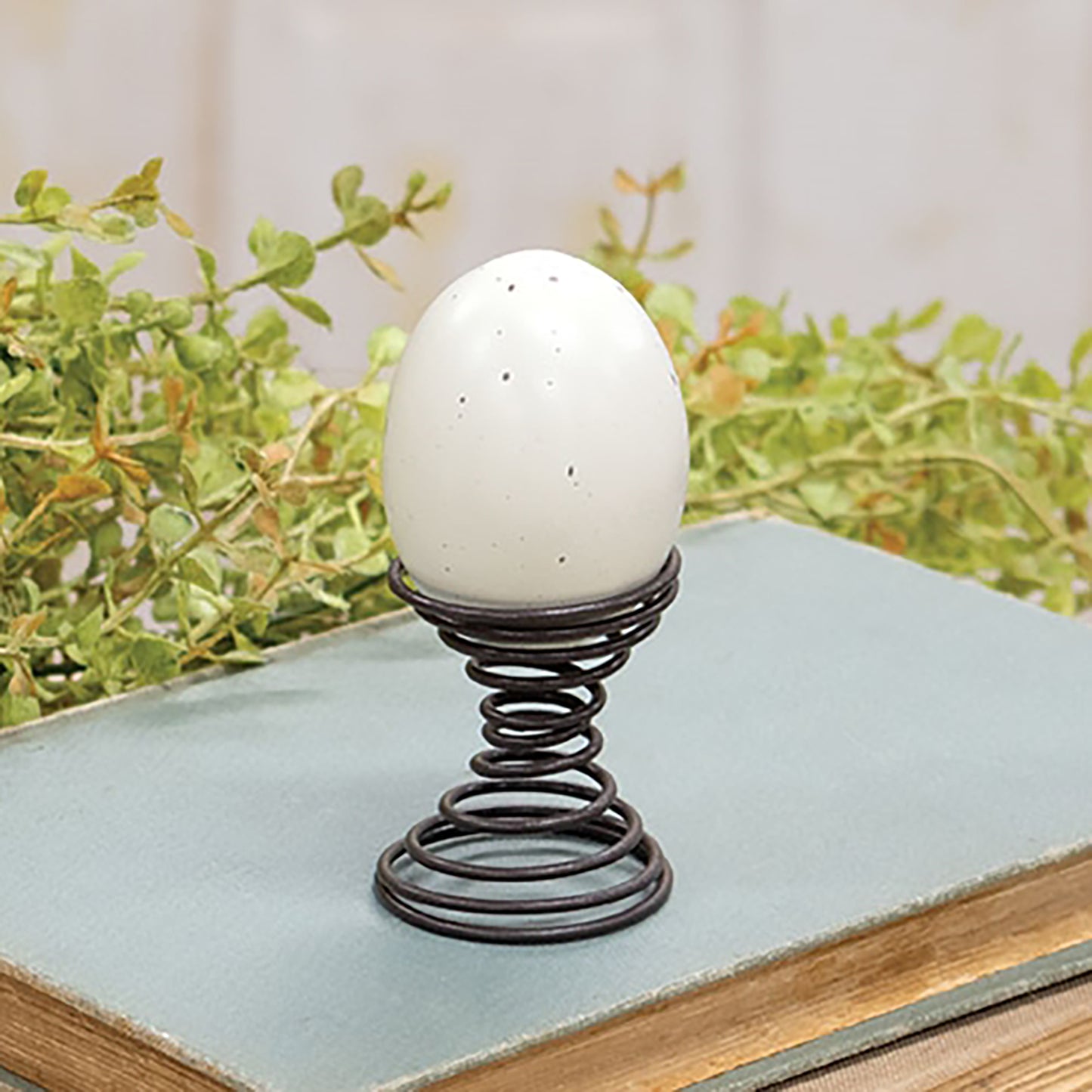 White egg on a decorative stand with greenery in the background