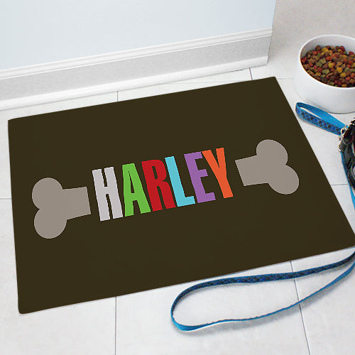 Dog bone pet mat with the name HARLEY printed inside a bone graphic, shown on a soft fleece surface with bound white edges.