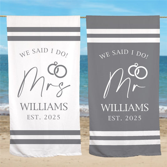 Personalized gray striped beach towel with "Mr." or "Mrs." text and family name, displayed on sandy beach background – 100% cotton honeymoon gift