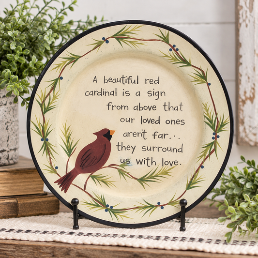 Round decorative ceramic plate displayed on small black stands, featuring a red cardinal perched on a leafy branch with the text, 'A beautiful red cardinal is a sign from above that our loved ones aren't far.