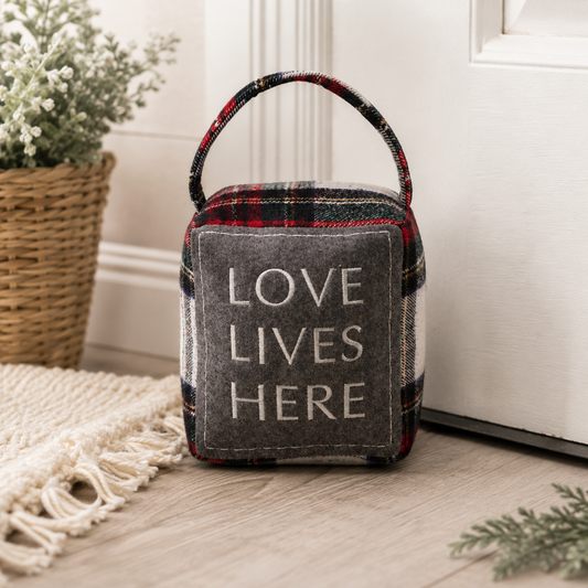 Love Lives Here weighted plaid doorstop in red, gray, black, white, and green flannel with embroidered dark gray felt patch and fabric handle.