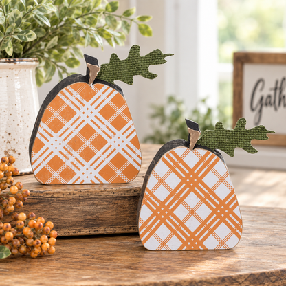 Two decorative pumpkin-shaped wooden ornaments with orange and white plaid patterns and green leaves, displayed on a wooden surface in a styled home setting.
