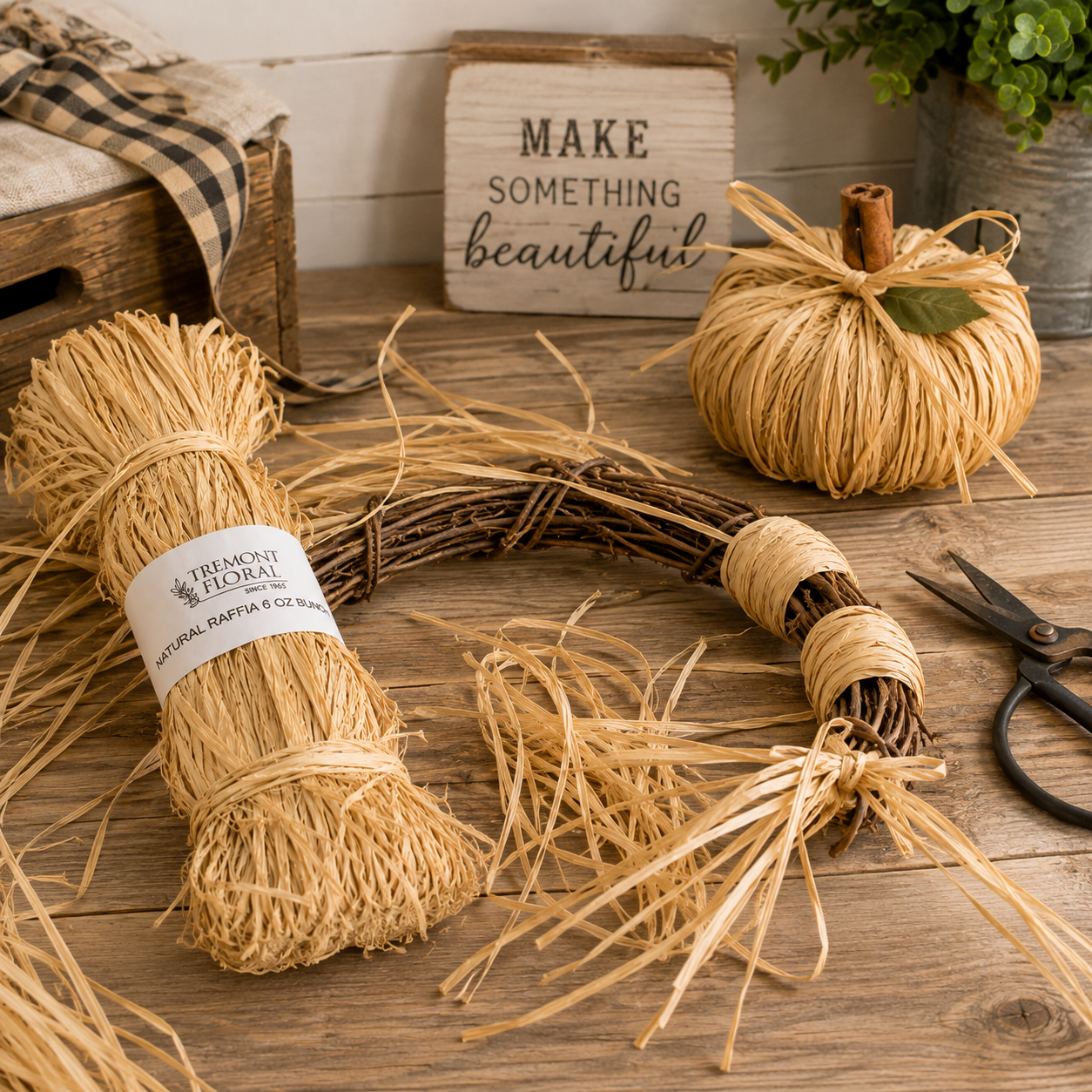 A rustic fall-themed wreath and decorative bundle made from natural jute twine, displayed on a wooden table with scissors, a small wrapped pumpkin, and a sign in the background.