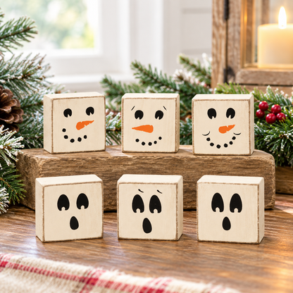 Six small wooden decorative blocks with simple black face drawings and orange carrot noses, arranged on a wooden surface with holiday greenery and a lit candle in the background.