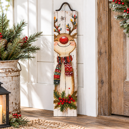 A vertical rustic wooden Christmas sign featuring a smiling reindeer with a red nose, colorful antlers, a red patterned scarf, and green holly with red berries at the bottom, displayed on a porch next to holiday greenery and a lantern.