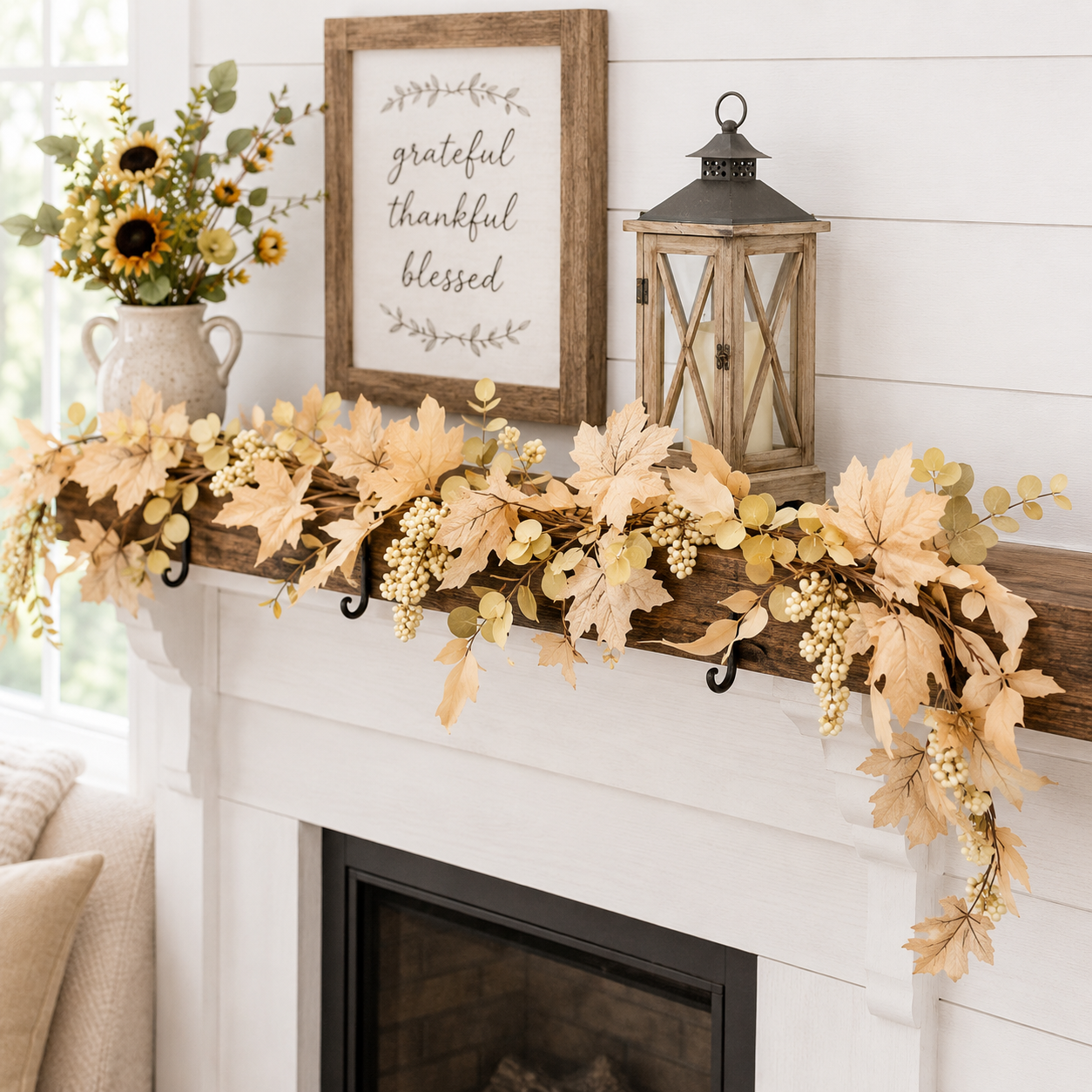 A rustic fall garland with beige leaves, white berries, and eucalyptus draped over a white fireplace mantel, styled with a framed sign reading 'grateful thankful blessed' and a wooden lantern.
