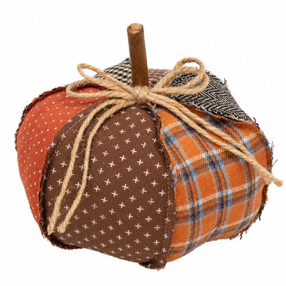 A handmade fabric pumpkin decoration with a wooden stem, featuring three distinct fabric panels: rust orange with white polka dots, medium brown with small white cross patterns, and orange with blue and white plaid. It is tied with a rustic jute twine bow.