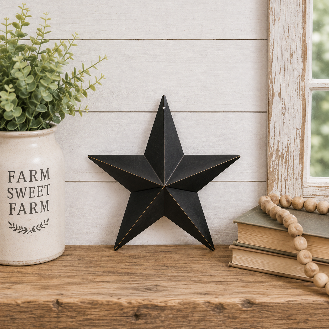 A black metal five-point star wall decor piece displayed on a rustic wooden shelf next to a white ceramic 'Farm Sweet Farm' planter and a stack of books with a wooden bead garland.