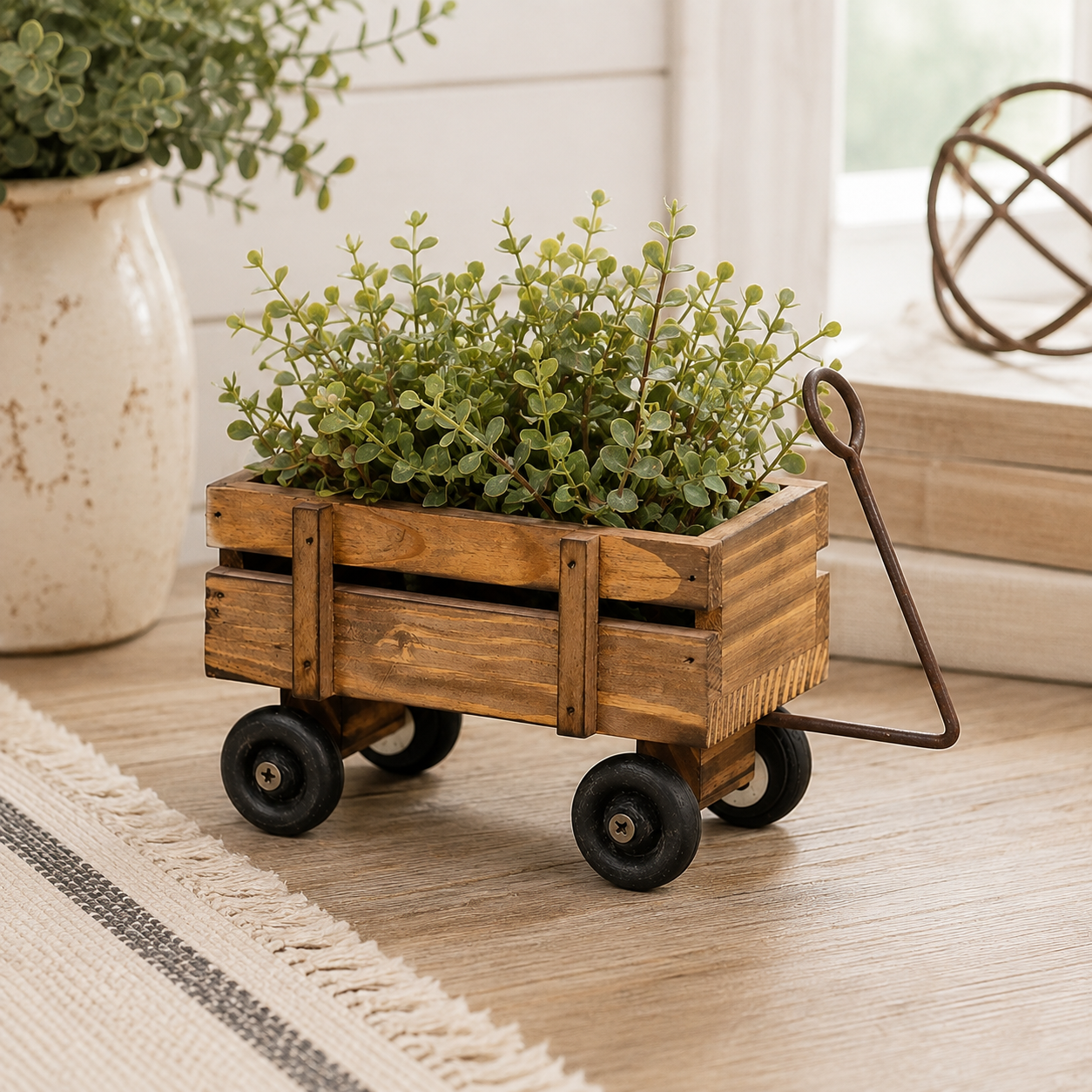 A small wooden planter styled like a rustic wagon with black wheels and a metal handle, filled with green leafy plants, placed on a light wood floor in a bright indoor setting.