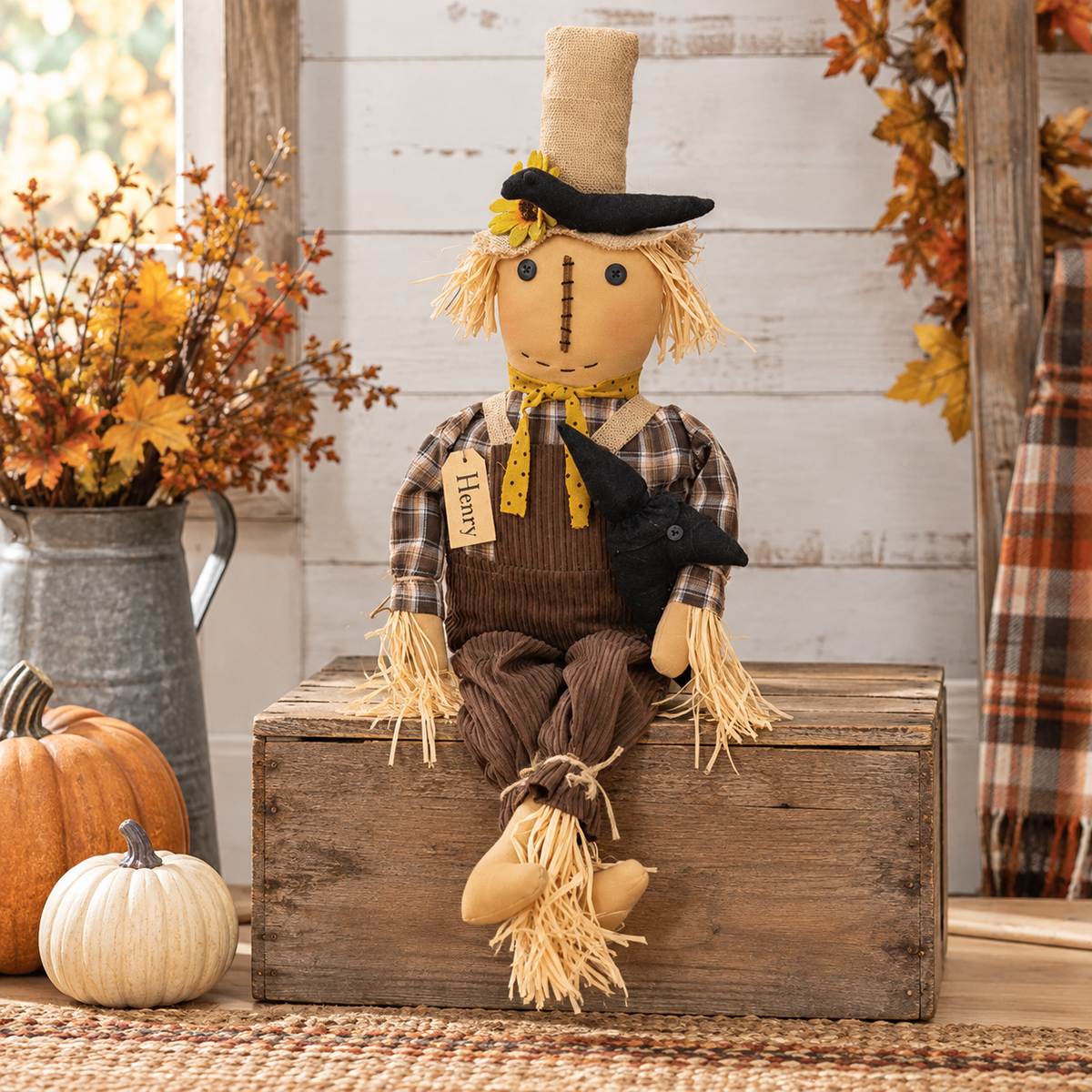 A rustic autumn-themed fabric scarecrow doll sits on a wooden crate. The scarecrow has straw hair, a black hat, a plaid shirt, brown overalls, and holds a black bird.