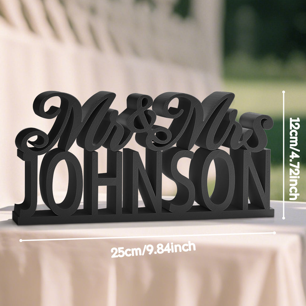 A view of the black 3D printed "Mr. & Mrs." table sign with overlay text indicating the product's side, showcasing the sleek design and customizable last name option.