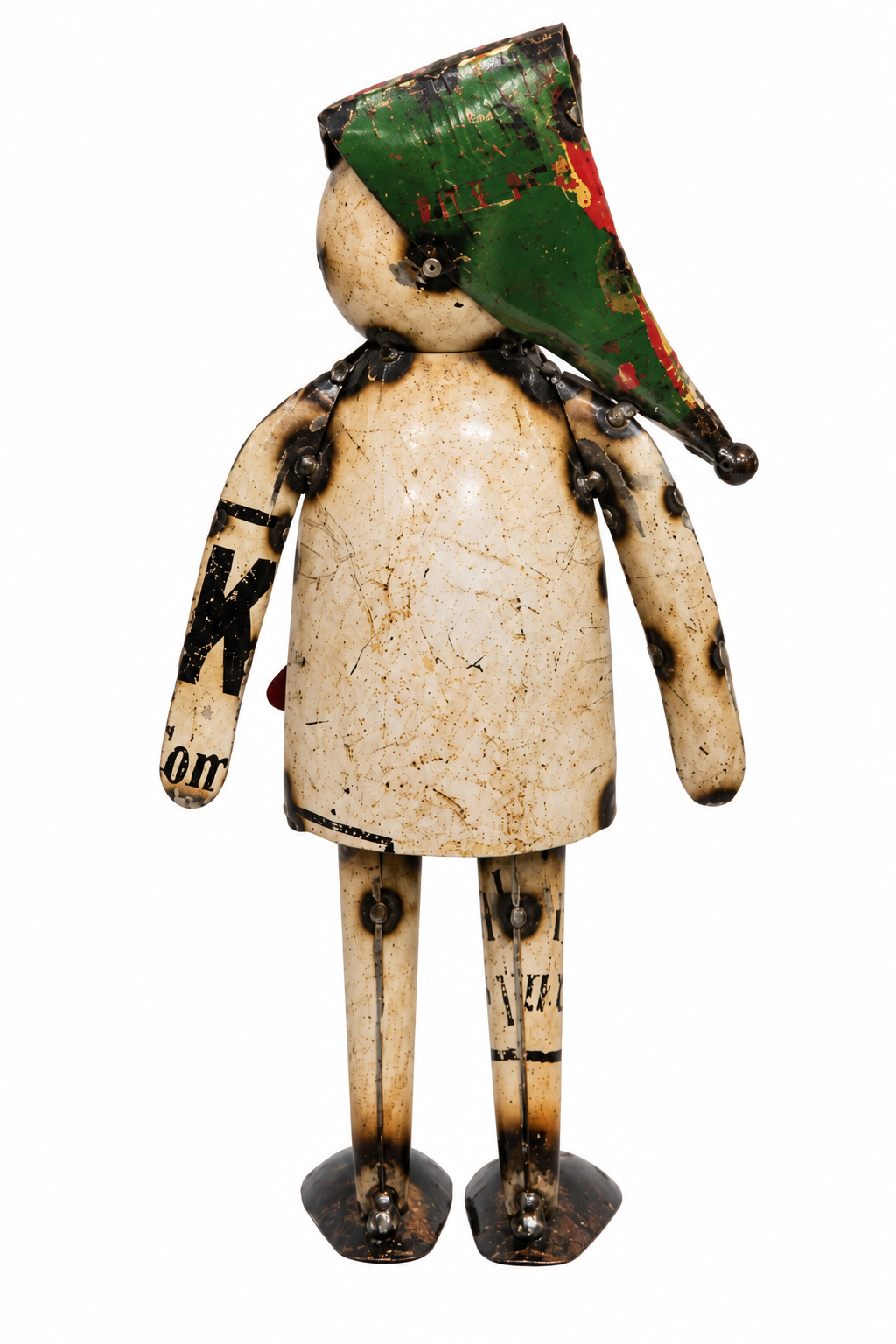 A rustic, handmade wooden doll figurine with a weathered cream-colored body, dark metal joints, and a green hat with red and black paint details, isolated on a white background.