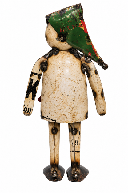 A rustic, handmade wooden doll figurine with a weathered cream-colored body, dark metal joints, and a green hat with red and black paint details, isolated on a white background.