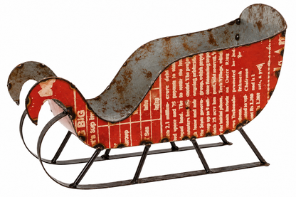 A vintage-style metal sleigh decoration with a rusted gray metal frame and runners, featuring a red side panel printed with white text and a weathered red-and-white front panel.