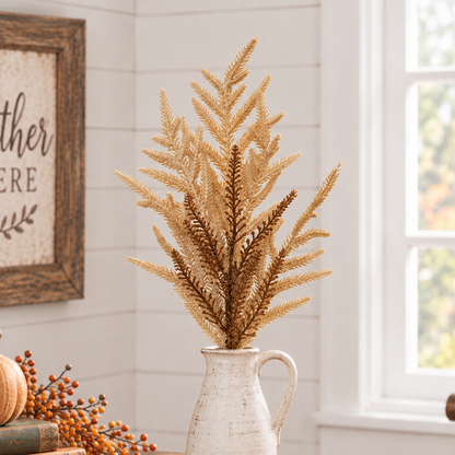 A decorative artificial fern arrangement in a white ceramic pitcher vase, styled on a rustic wooden table with autumn books, a small pumpkin, and berries in a bright room with a window and framed sign.