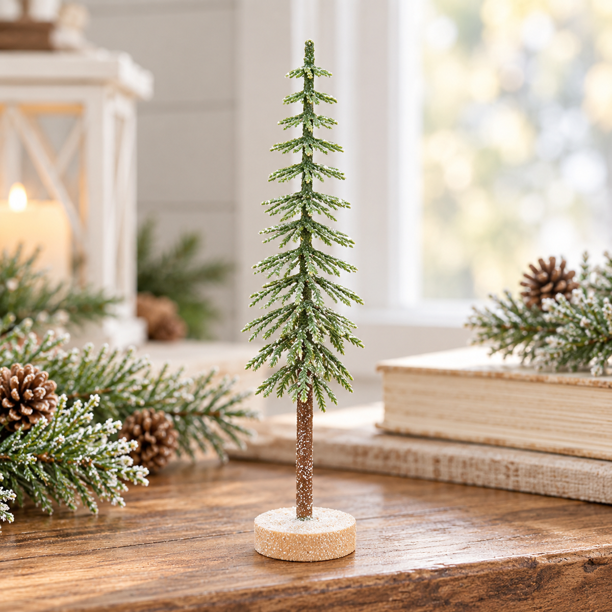 A small decorative evergreen tree ornament with a glittery green textured body and a brown trunk on a round cork base, displayed on a wooden table with holiday decor in a softly lit indoor setting.