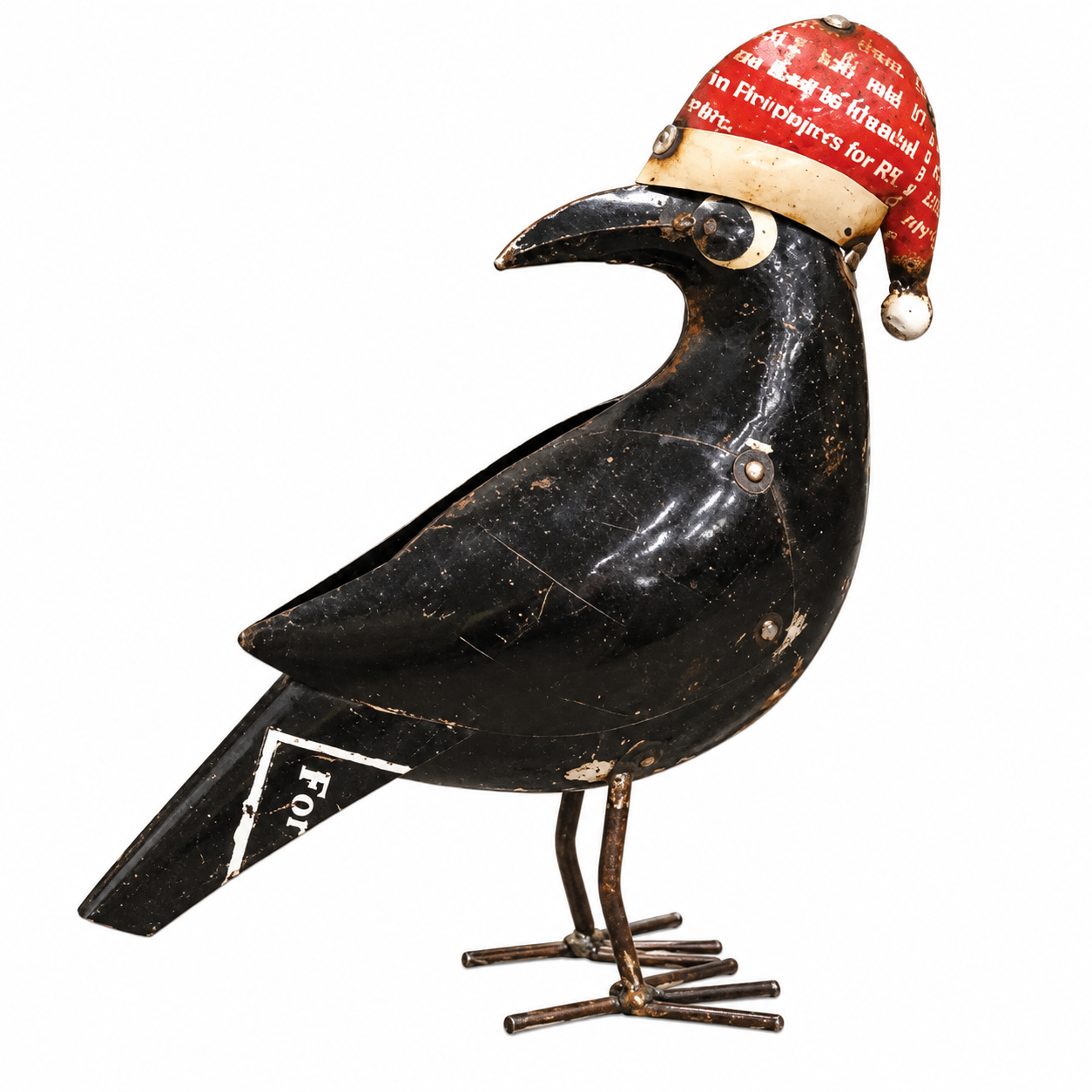 A vintage black metal bird figurine, likely a crow or raven, wearing a red Santa hat with white text. The bird has a glossy black finish with visible wear, scratches, and peeling paint, and stands on thin metal legs against a plain white background.