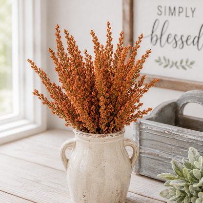 A rustic ceramic pitcher vase filled with dried orange-brown decorative grasses, styled on a light wood surface next to a distressed gray wooden crate and a sign that reads 'SIMPLY blessed'.