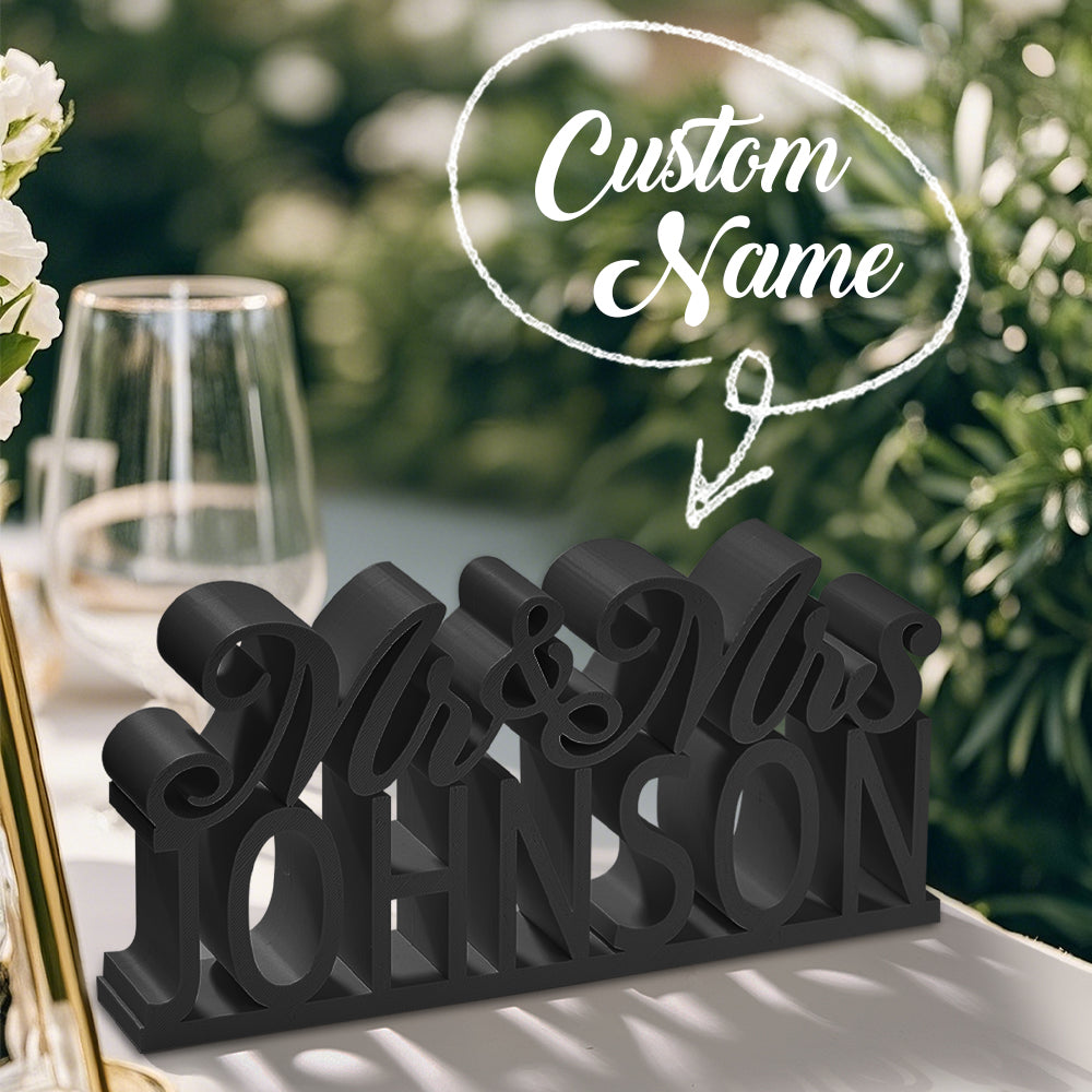 A 3D printed "Mr. & Mrs." table sign in black, with overlay text indicating the customizable last name option for a personalized design.