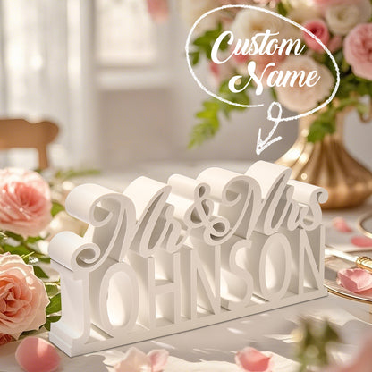 A white 3D printed "Mr. & Mrs." table sign with overlay text indicating the customizable last name option for a personalized design.