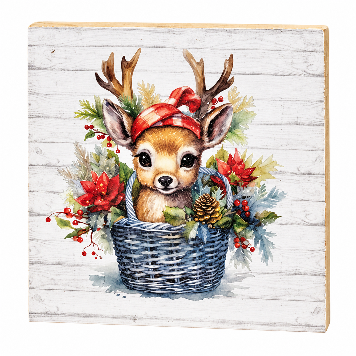 A square decorative sign or plaque with a rustic white wood-plank background featuring a painted illustration of a baby deer with antlers sitting in a blue basket, surrounded by red berries, green foliage, a red plaid headband, and a pinecone.