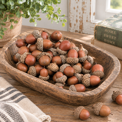 A wooden bowl filled with real acorns on a rustic wooden table, with a potted plant and old books in the background.