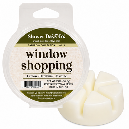 A 2 oz round plastic tub of Slower Days Co. 'window shopping' lemon gardenia jasmine coconut soy wax melts, shown next to three pale cream wax melts on a white background.