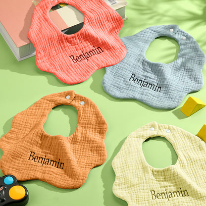 Four vibrant colors of personalized baby bibs on display: blue, yellow, orange, and brown. Custom embroidery options available for each color.