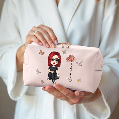 A woman holding a pink personalized makeup bag, featuring a custom avatar or cartoon character, birth flower, and name, highlighting the personalized design and color options.